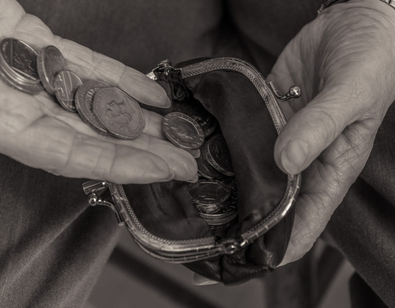 British pensioner putting coins into a purse. Close up of hands. Black and white image. Cost of living concept.