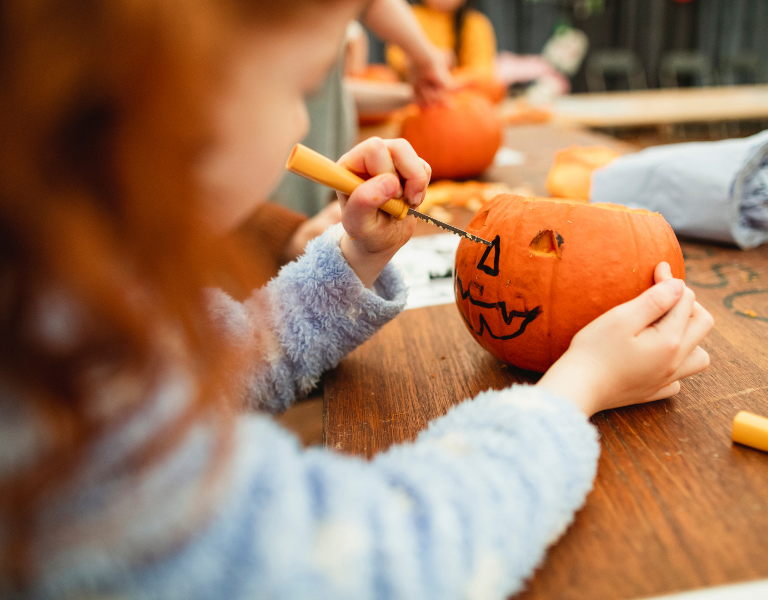 A stock photo showing a young girl with red hair painting a pumpkin at a family event