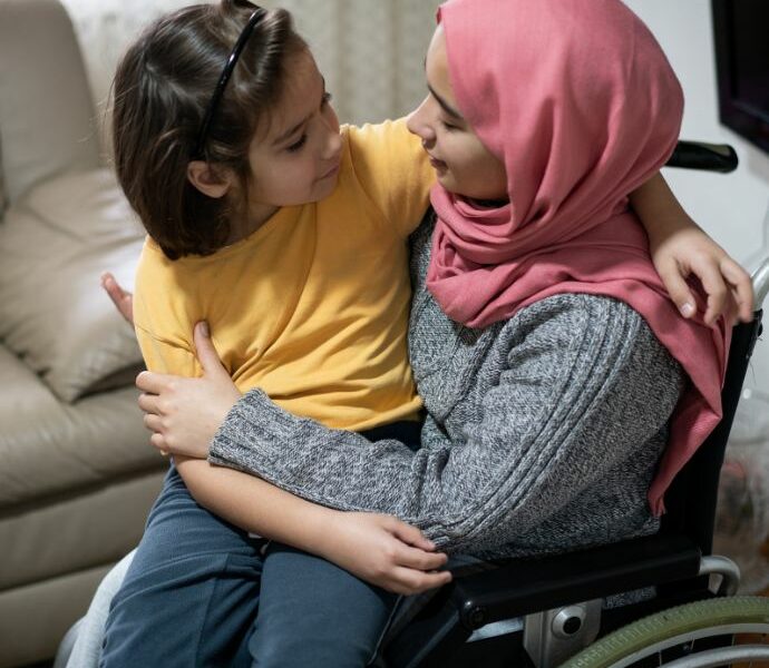 An image of a woman in a wheelchair with a young girl sitting on her knee (c) Carers Trust